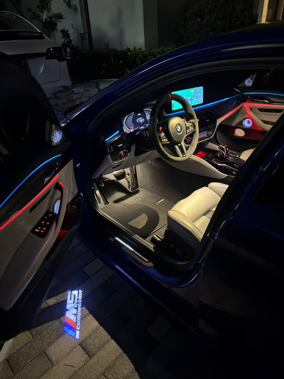 Close-up of an M5 Competition logo projected beside the driver's door of a BMW M5